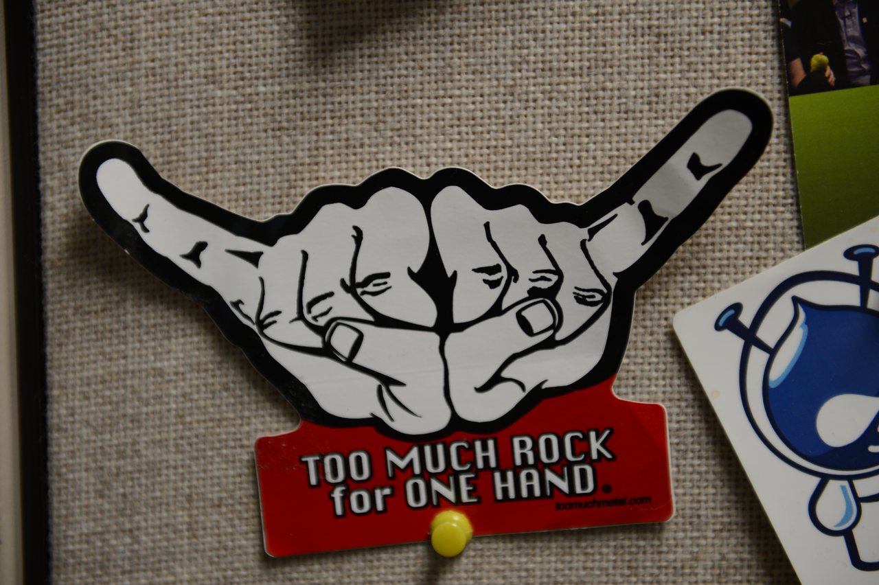 Sticker on a bulletin board showing two hands making a rock sign with the text "Too much rock for one hand.
