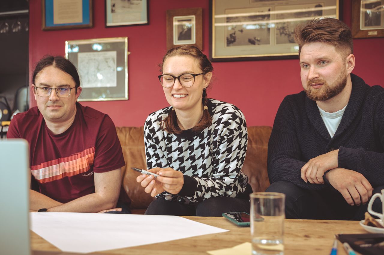 Three people are seated on a sofa, with a blank sheet of paper in front of them.