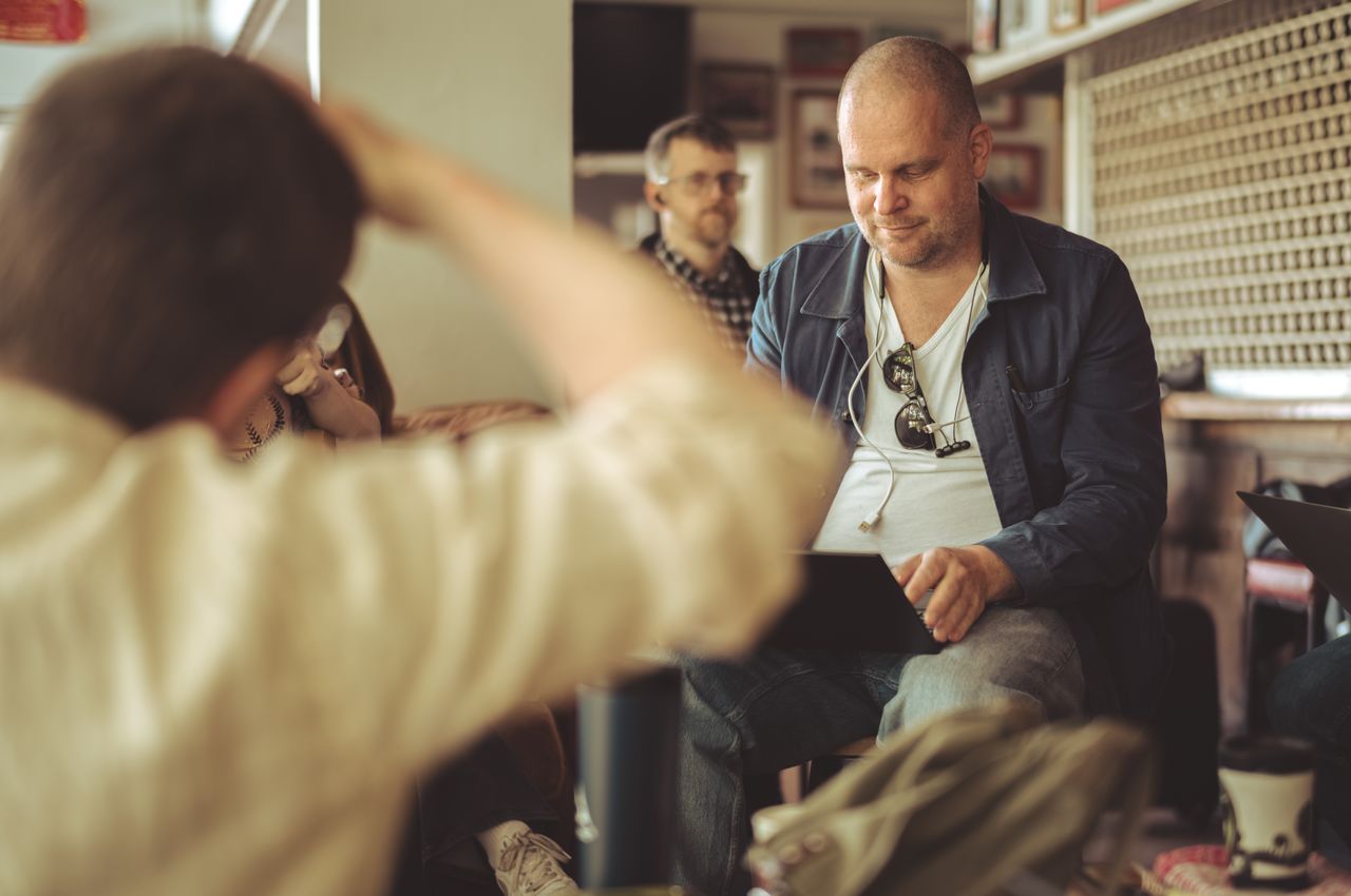 A man is sitting in a chair with his laptop on his lap, diligently taking notes.