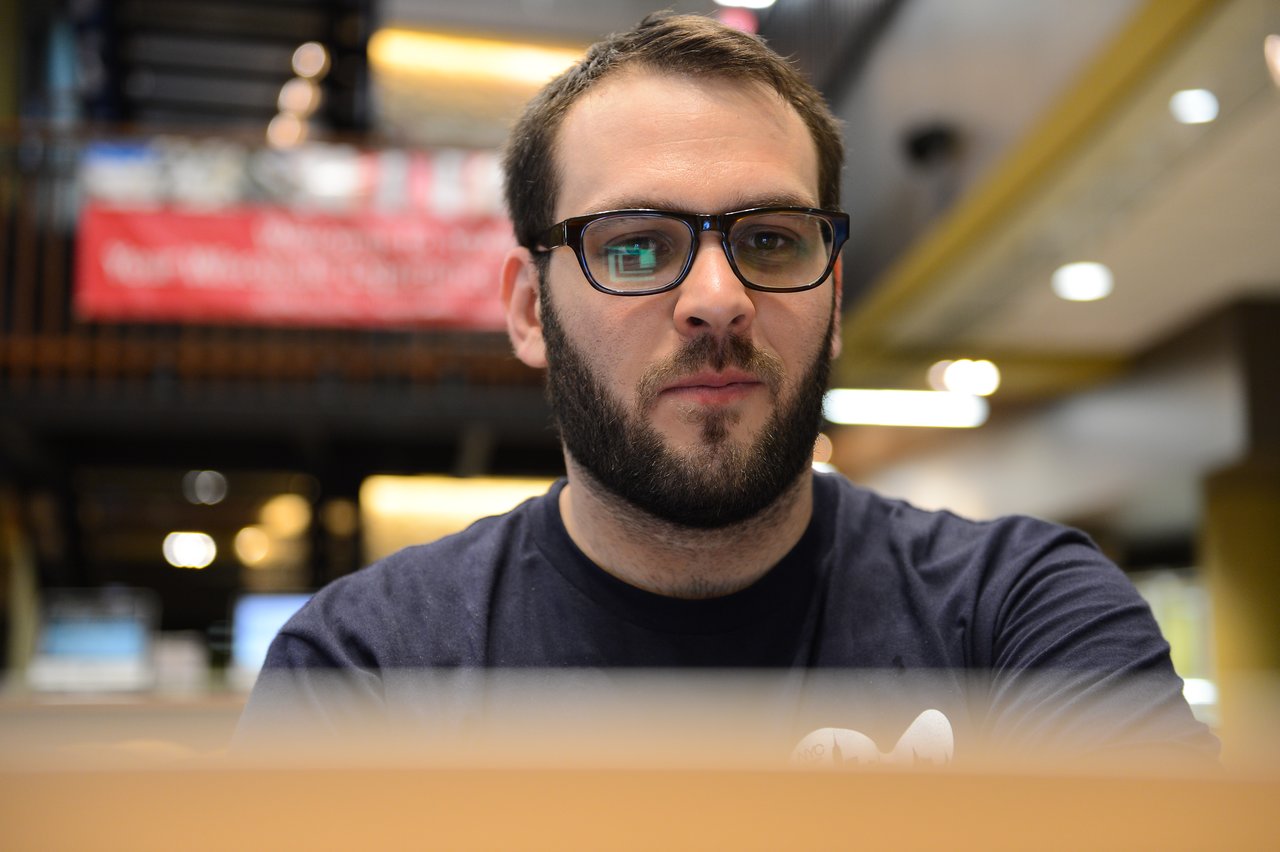 A person with glasses and a beard is focused on working at a laptop during a coding sprint.