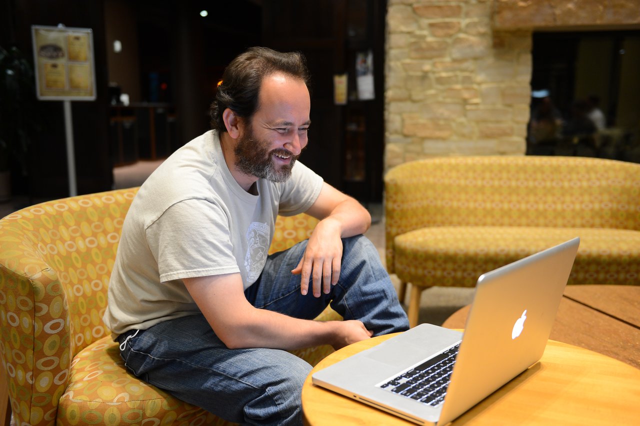 A man sits in a chair, smiling while working on a laptop during a Drupal developer sprint.