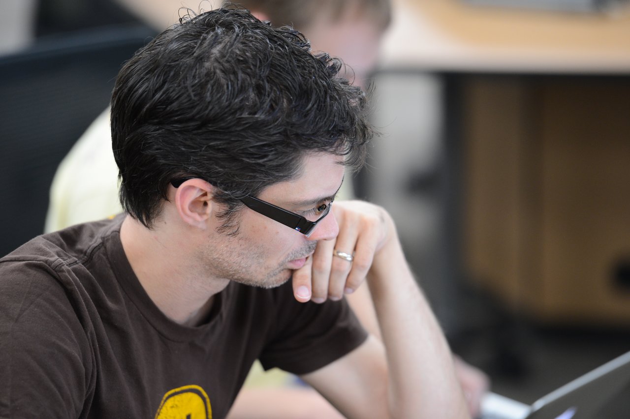 A person wearing glasses and a brown shirt is focused on a laptop during a coding sprint.