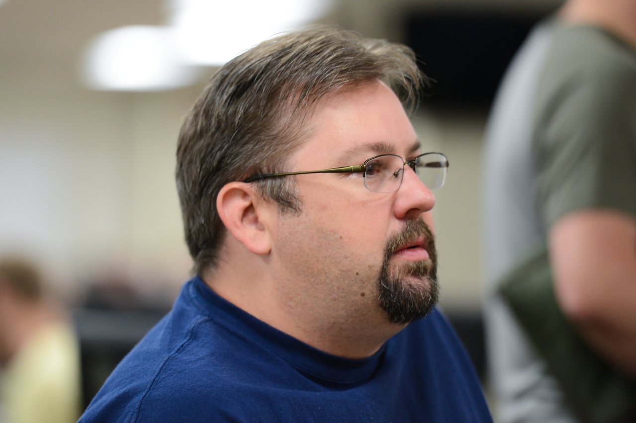 A man in glasses and a blue shirt listens attentively during the Drupal Developer Summit sprint event.