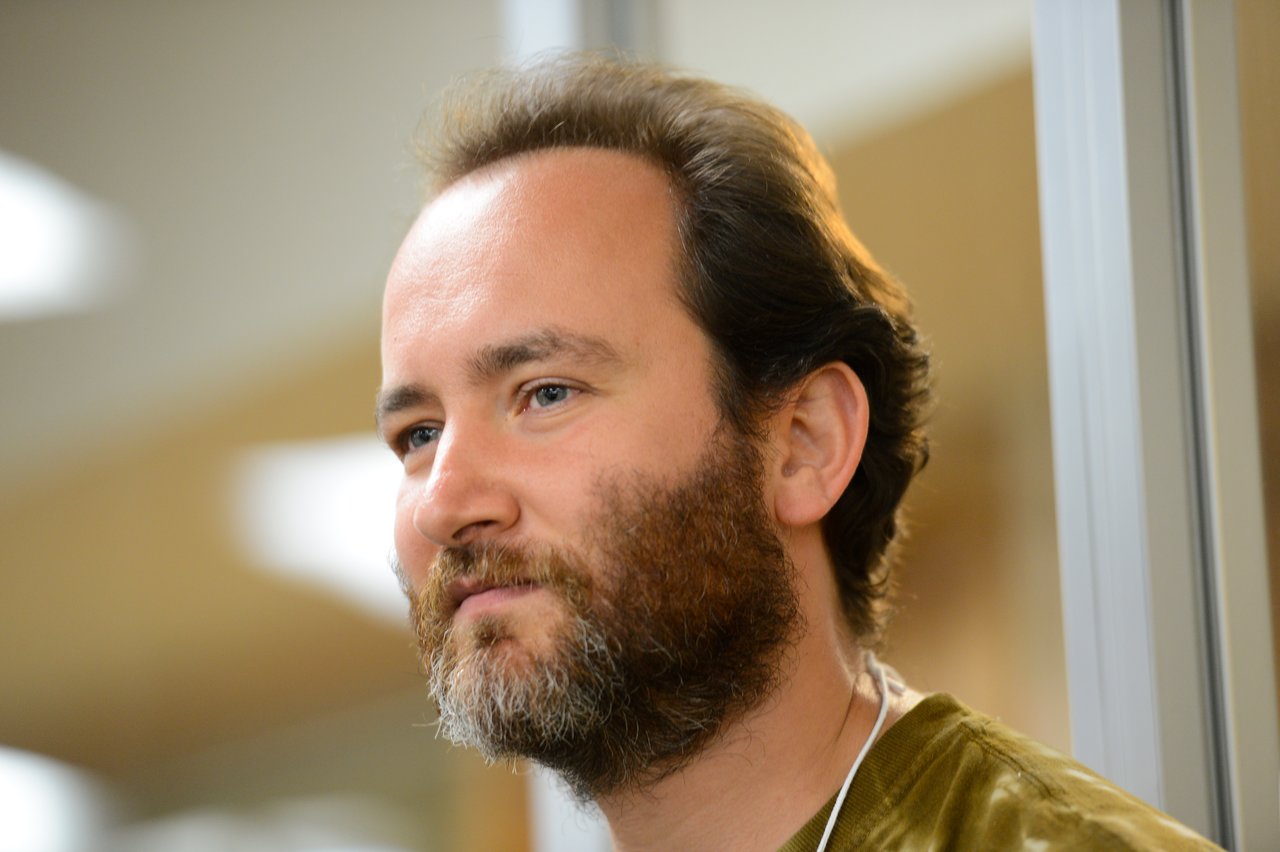 A bearded man wearing a lanyard looks focused during the Drupal Developer Summit in Madison, 2012.