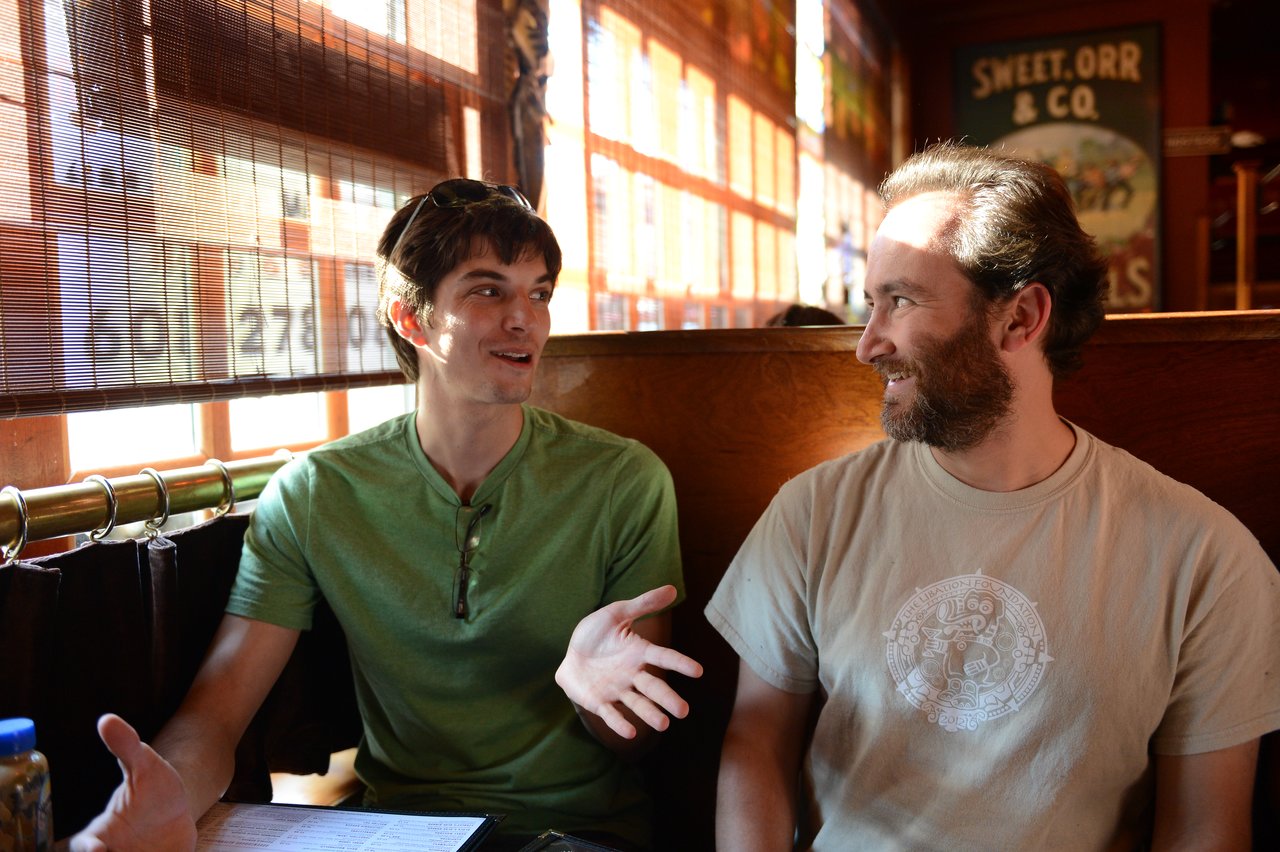 Two people sitting in a booth, engaged in a conversation, with one gesturing while speaking.