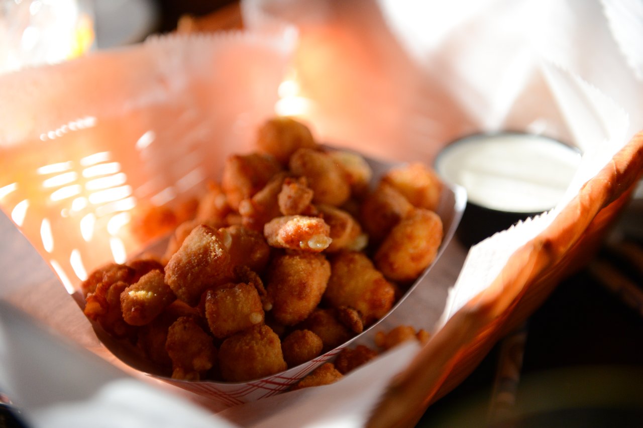A basket of fried cheese curds with a cup of dipping sauce on the side.