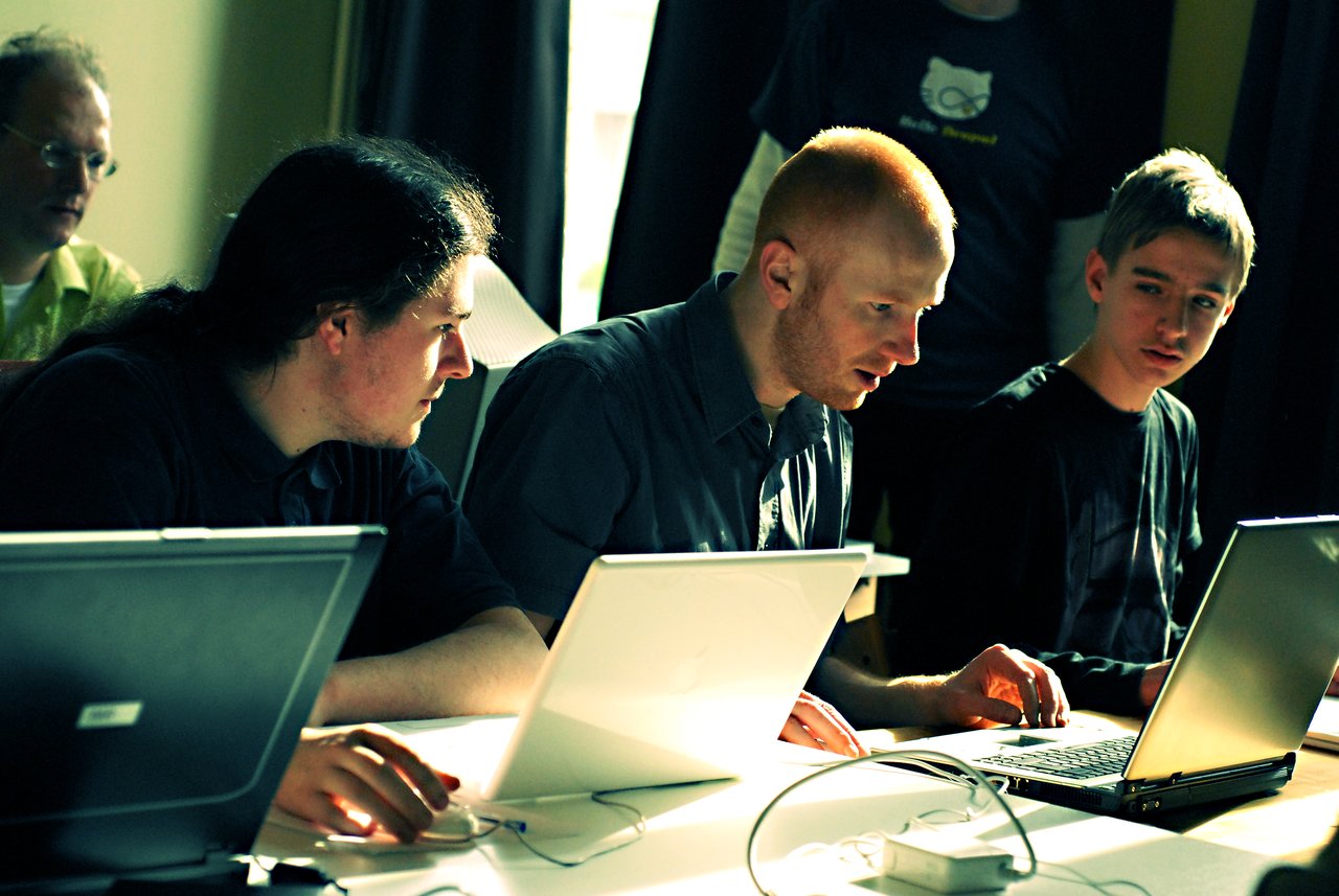 Three people sit at a table with laptops, attentively discussing something on the screen during a workshop.