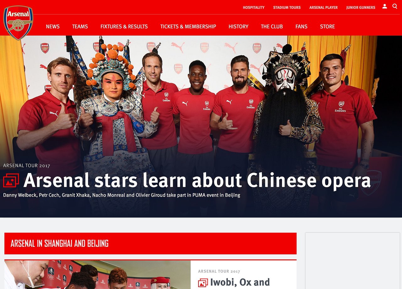 Arsenal players pose with Chinese opera performers at a cultural event in Beijing, wearing team shirts and smiling.