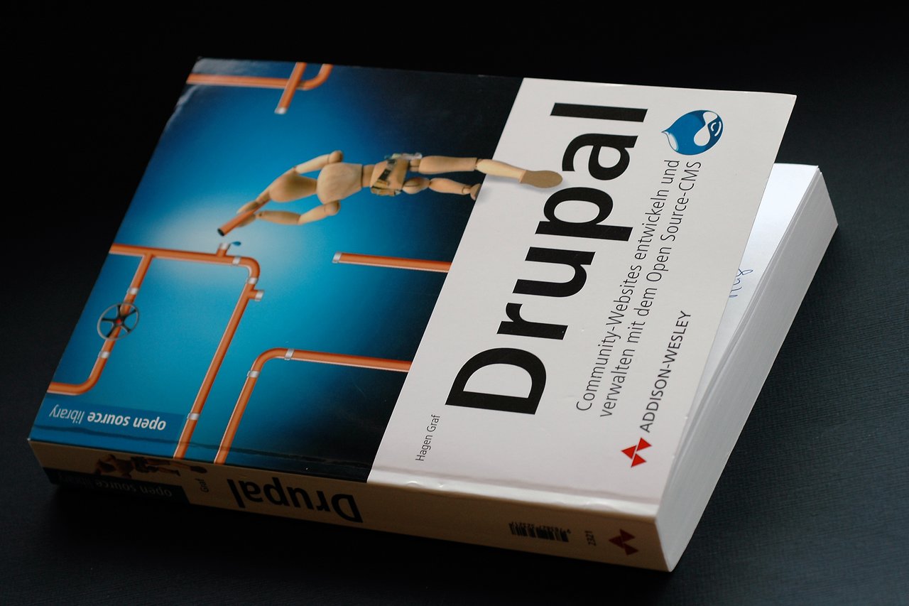 A Drupal book with a cover showing a wooden figure climbing pipes, placed on a dark surface.