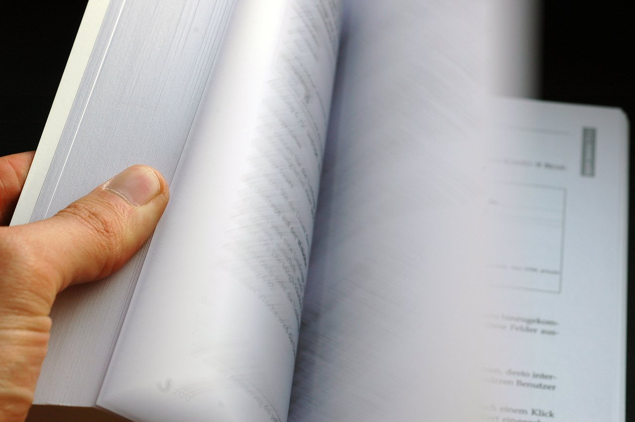 A person flips through the pages of a book, revealing printed text and diagrams on the open pages.