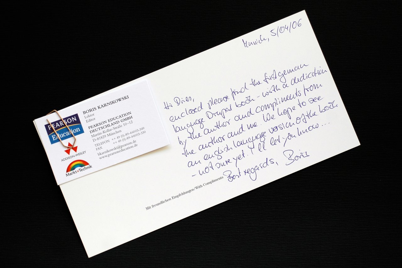 A handwritten note with a business card attached, discussing the first German-language Drupal book and its English version.