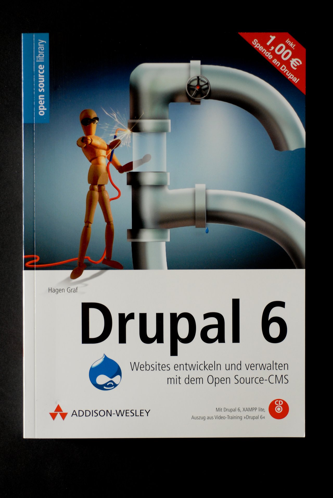 Cover of the book "Drupal 6" by Hagen Graf, featuring a robotic figure working on a large pipe structure.