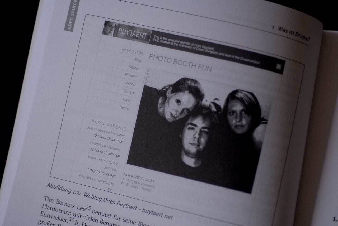 A book page displays a screenshot of a website featuring a black-and-white photo of three people posing together.