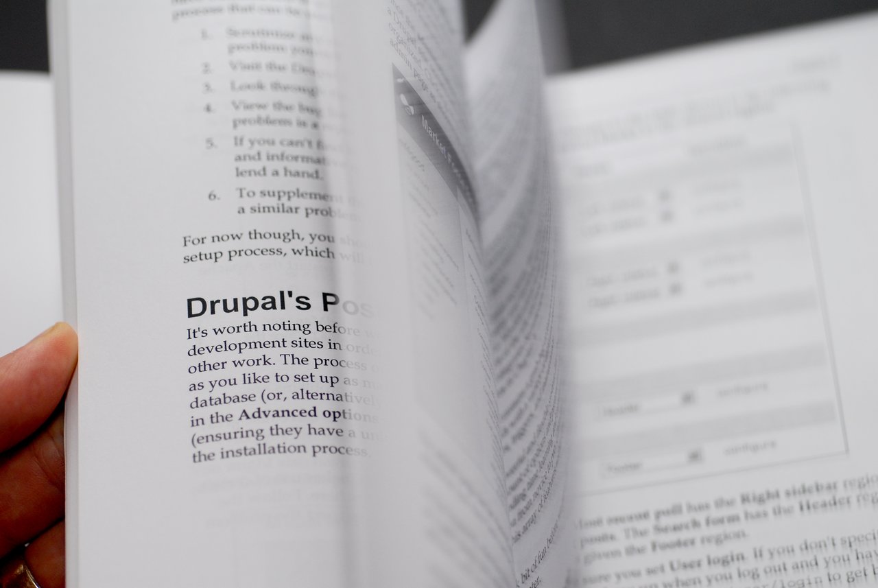 A person flips through a book about Drupal, with the world "Drupal" clearly visible on a page.