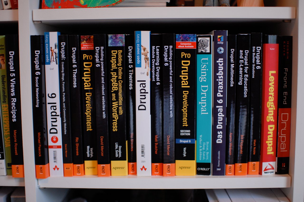 A bookshelf filled with various books about Drupal, including development, themes, and site-building guides.