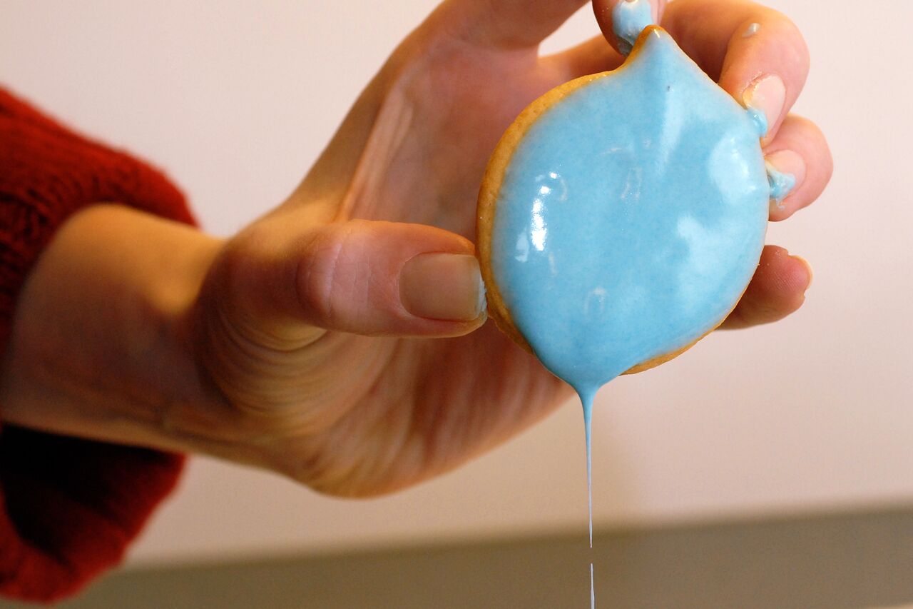 A hand holds a cookie covered in blue frosting, with excess frosting dripping off.