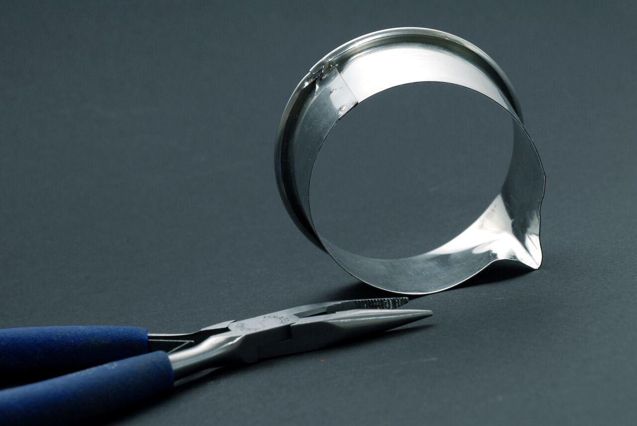 A metal ring is bent into the shape of the Drupal logo, with pliers resting nearby.