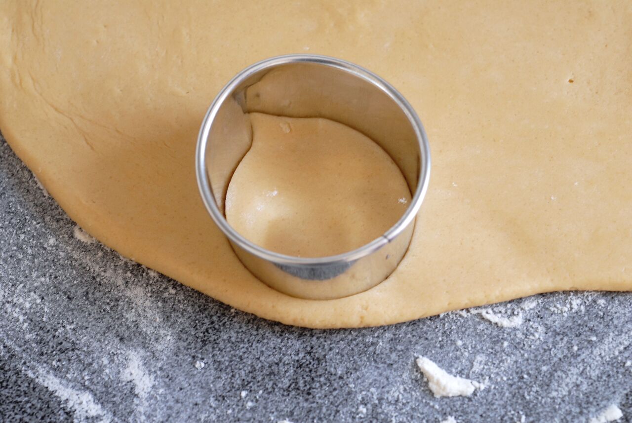 A round cookie cutter is pressed into rolled-out dough on a floured surface.