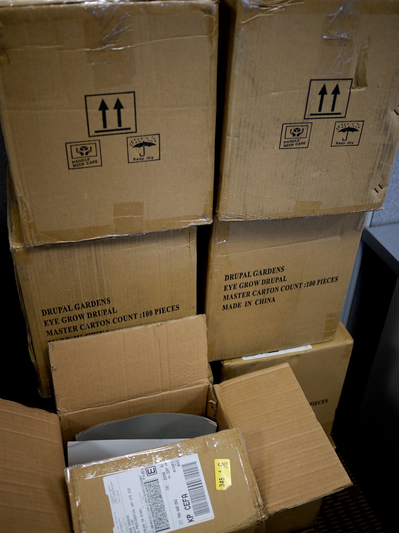 Several stacked cardboard boxes labeled "Drupal Gardens Eye Grow Drupal", with some boxes open revealing packing materials.