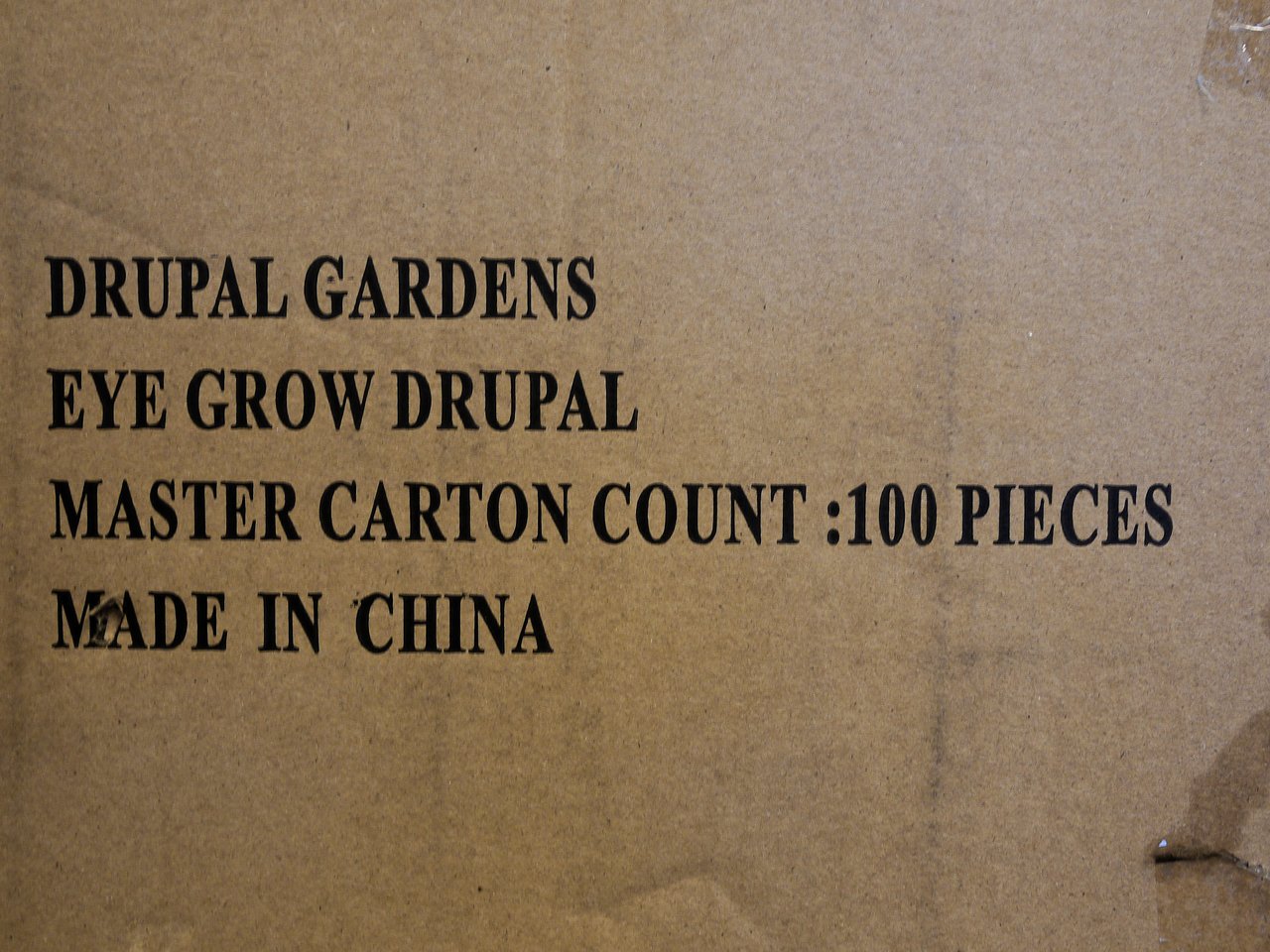 Text printed on a cardboard box reads: "DRUPAL GARDENS, EYE GROW DRUPAL, MASTER CARTON COUNT: 100 PIECES, MADE IN CHINA.