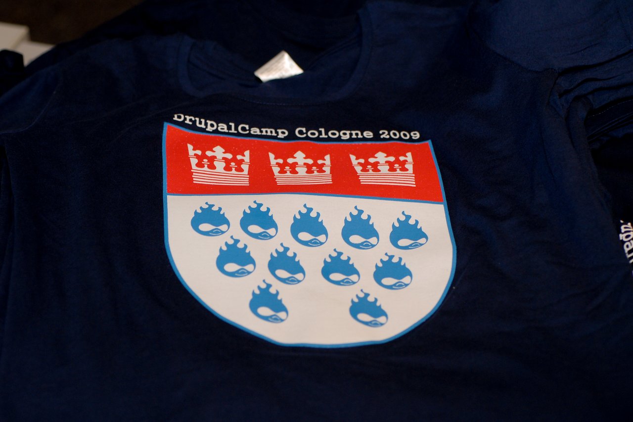Navy blue T-shirt with a DrupalCamp Cologne 2009 logo featuring a shield with crowns and flaming Drupal logos.