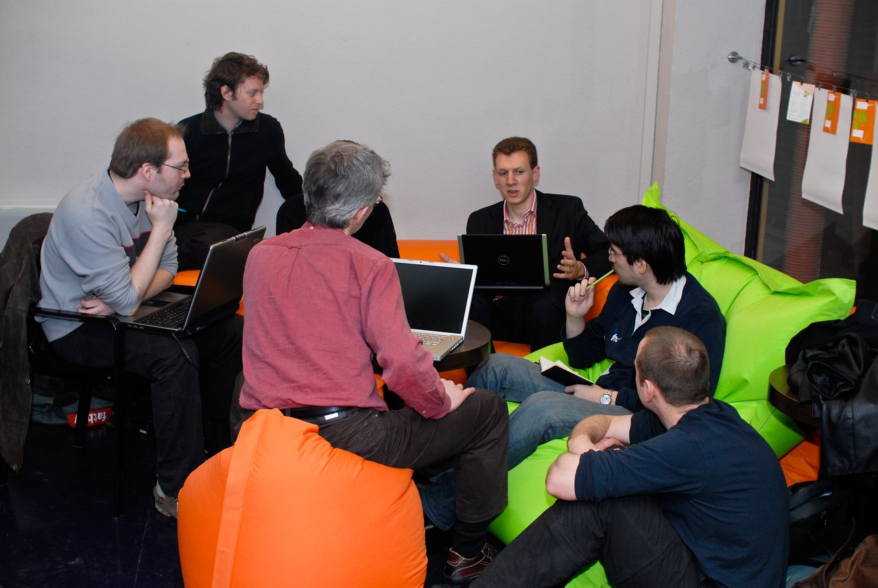 A group of people sitting on bean bags, discussing and using laptops at a DrupalCamp event.
