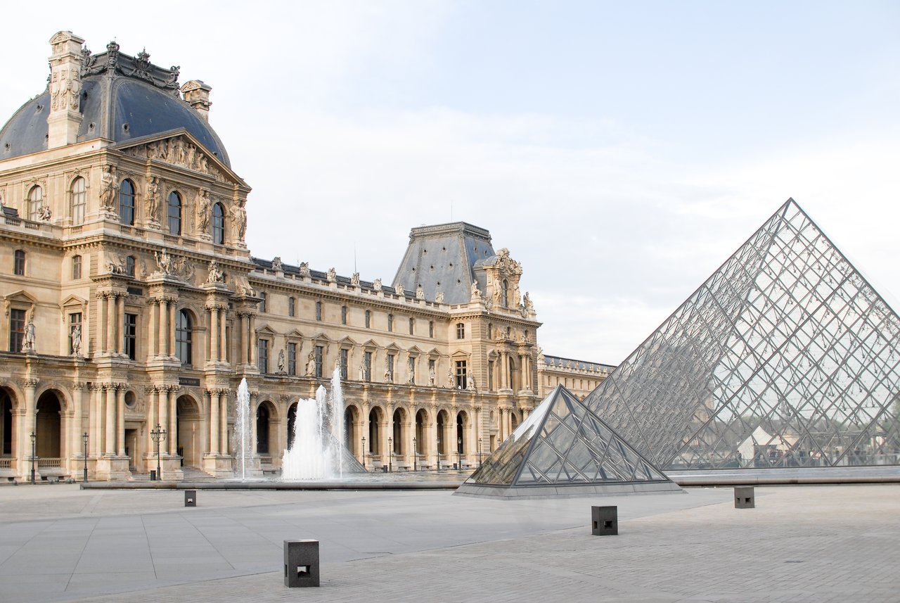 The Louvre Museum with its glass pyramid entrance and a water fountain in the foreground.