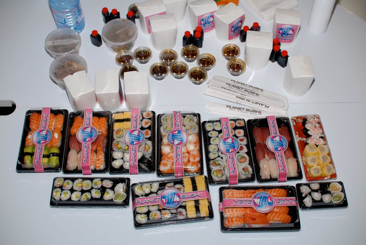 A table filled with sushi trays, soy sauce, chopsticks, and takeout containers from Planet Sushi, ready to eat.