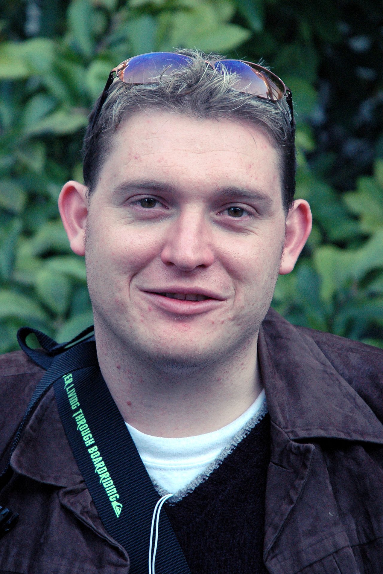 A person with short, light-colored hair and sunglasses on their head smiles slightly while looking at the camera.