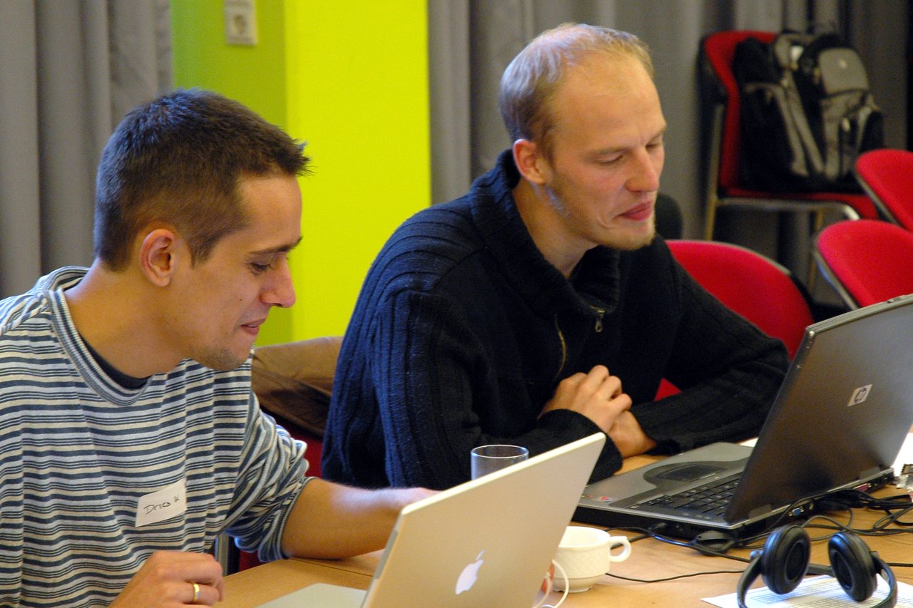 Two people sitting at a table, working on laptops and engaged in conversation at a Drupal conference.