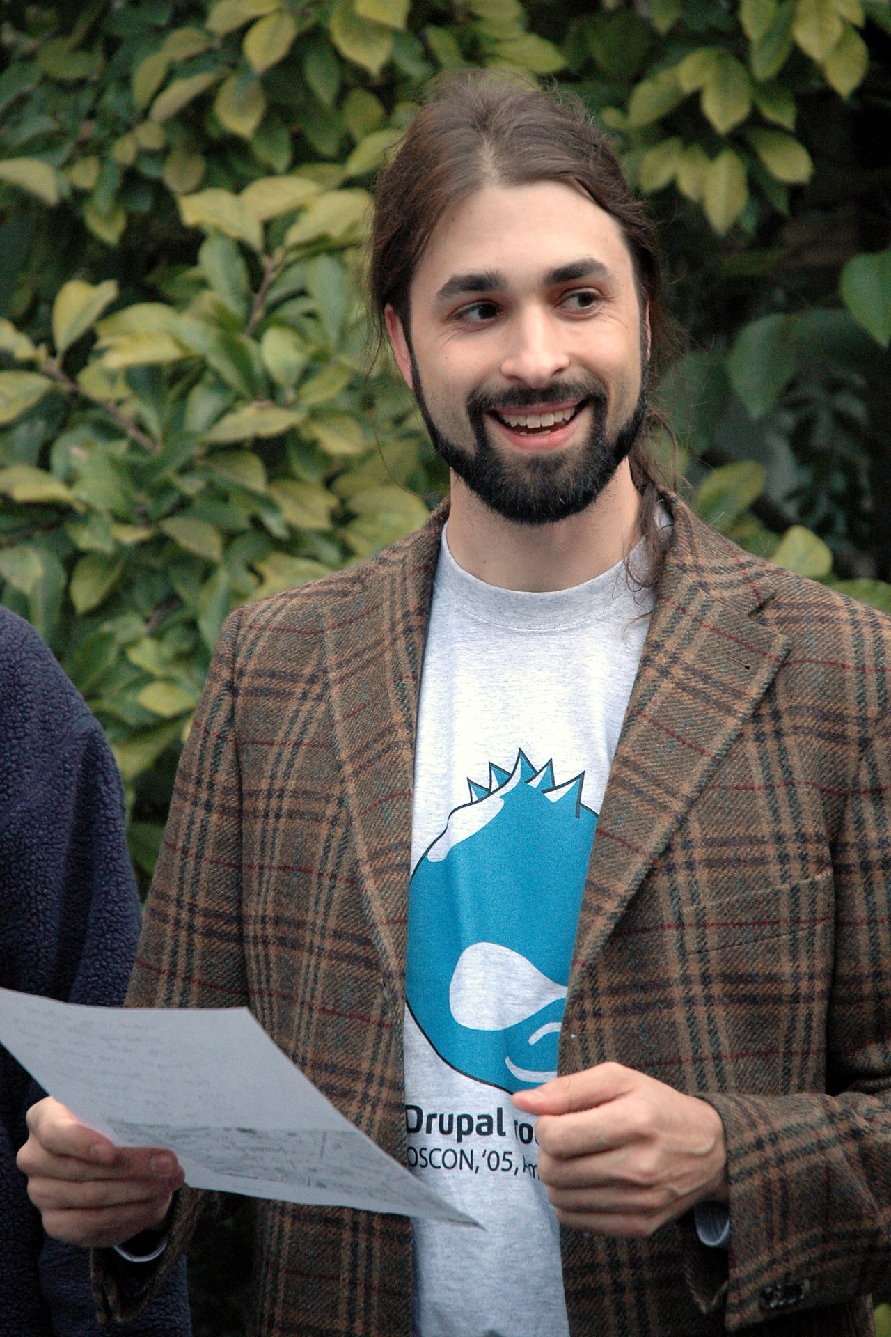A man with a beard and long hair smiles while holding a piece of paper at DrupalCon Amsterdam 2005.