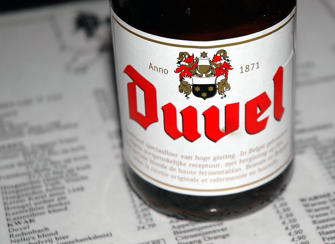 A close-up of a Duvel beer bottle with its label visible, placed on a printed menu.