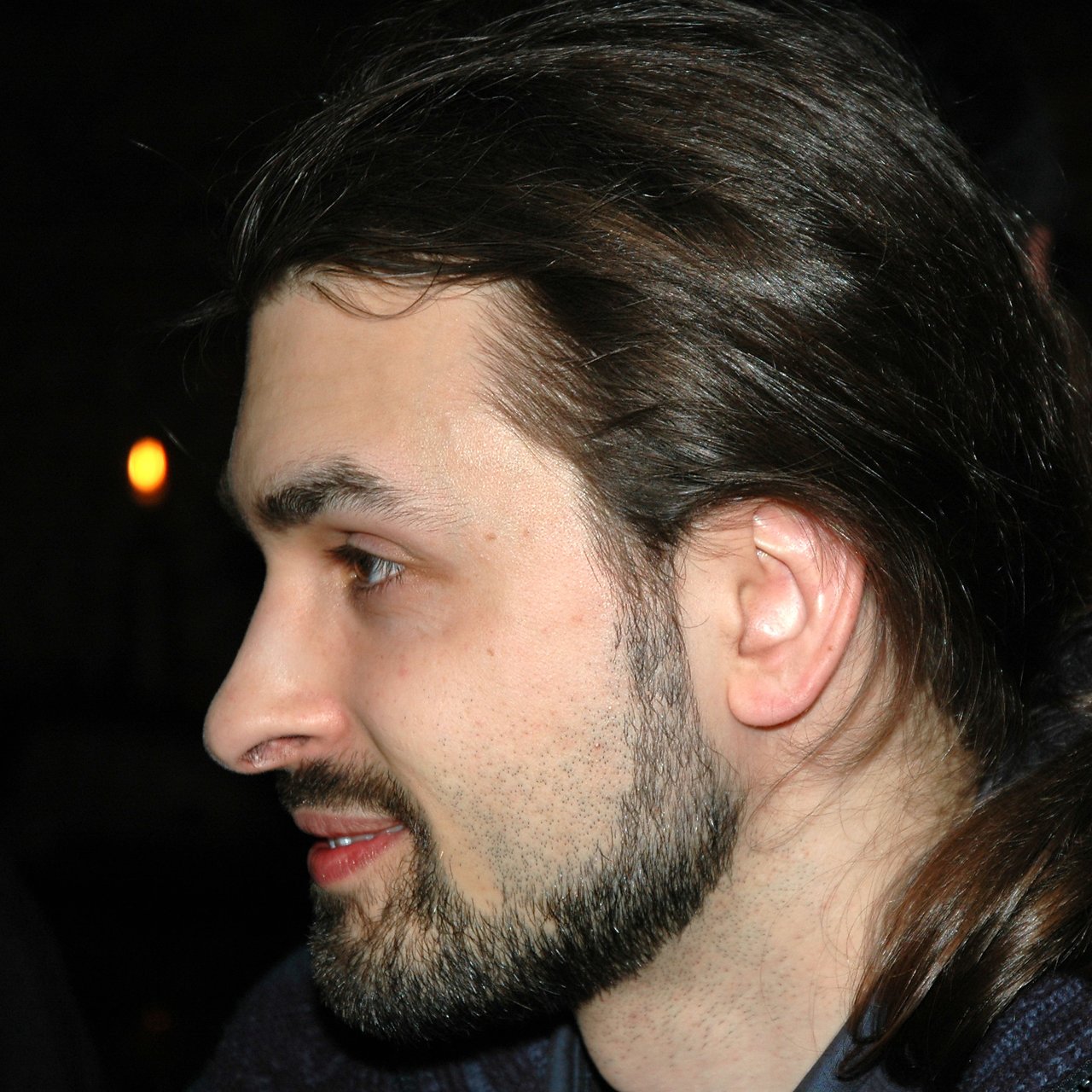 A person with long hair and a beard is shown in profile, looking to the left with a slight smile.