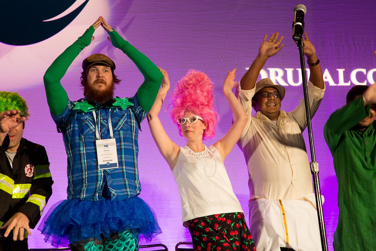 People in colorful costumes dance energetically on stage at the DrupalCon Baltimore 2017 prenote event.