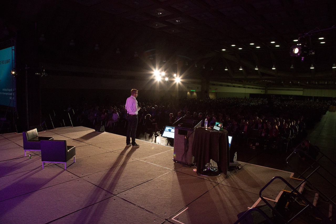 A speaker stands on a stage, addressing a large audience at DrupalCon Baltimore 2017.