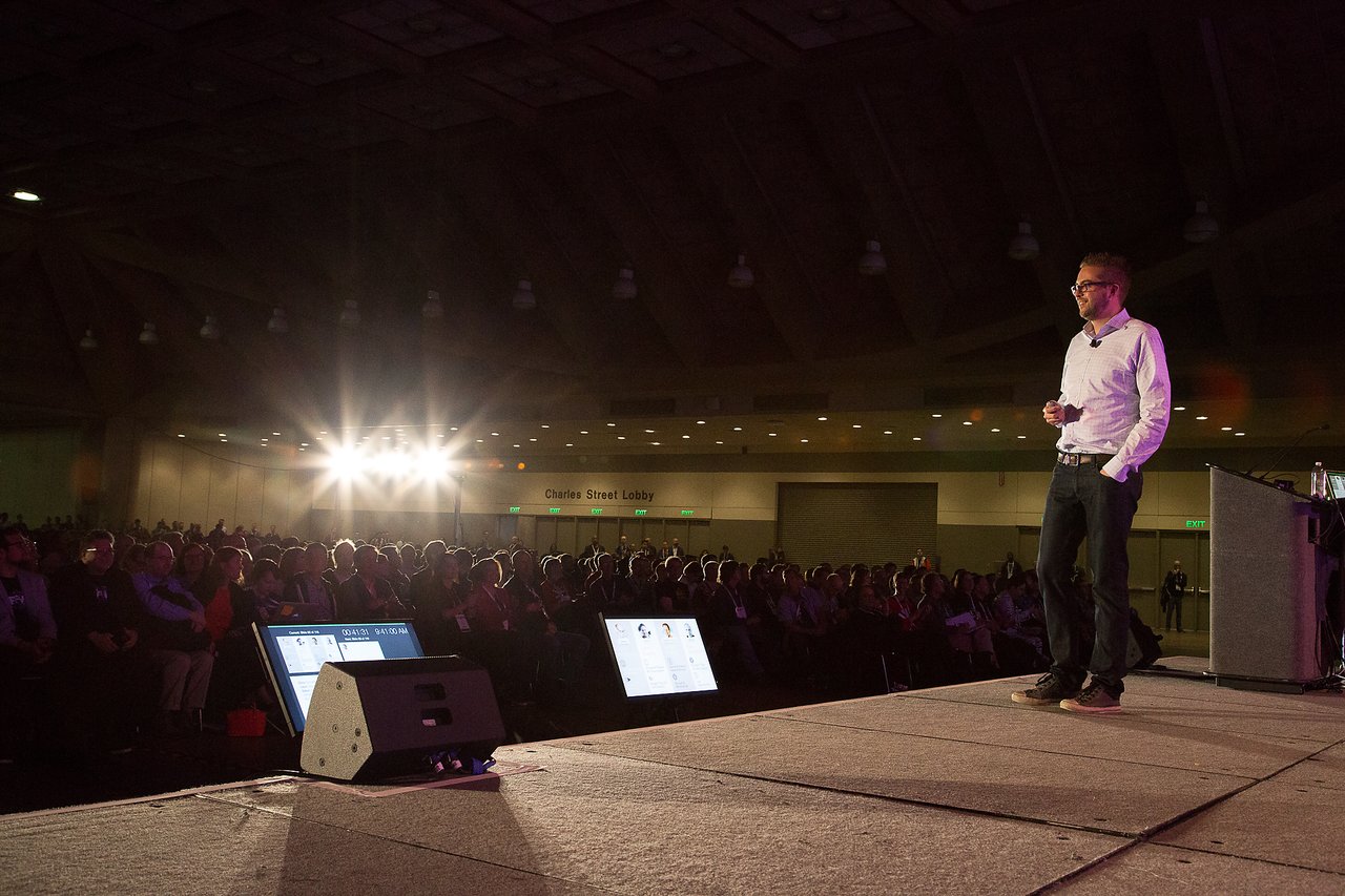 A speaker in a white shirt and jeans presents on stage to a large audience at DrupalCon Baltimore 2017.