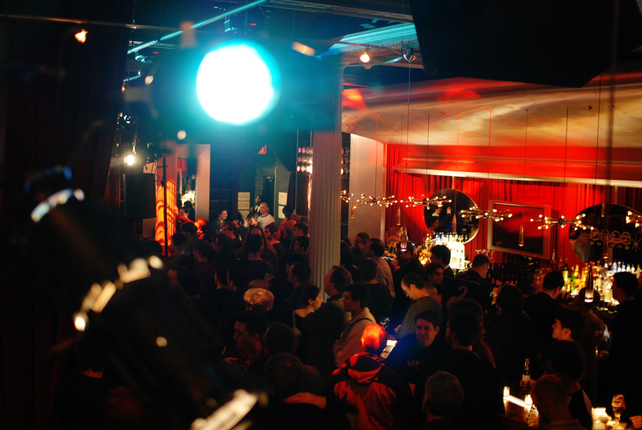 A large crowd gathers at a dimly lit bar for the Acquia launch party during DrupalCon Boston 2008.