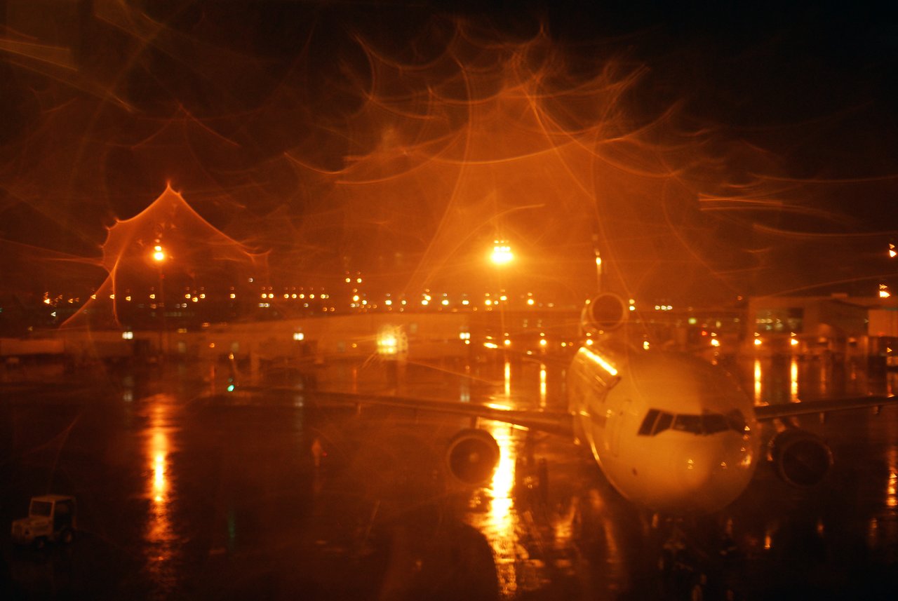 A parked airplane on a wet tarmac at night, with bright airport lights reflecting on the ground.