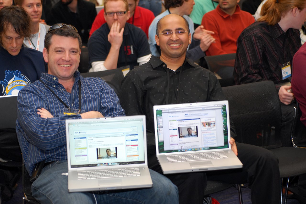 Two smiling AOL developers display their laptops, showcasing AOL's intranet built with Drupal at a conference.