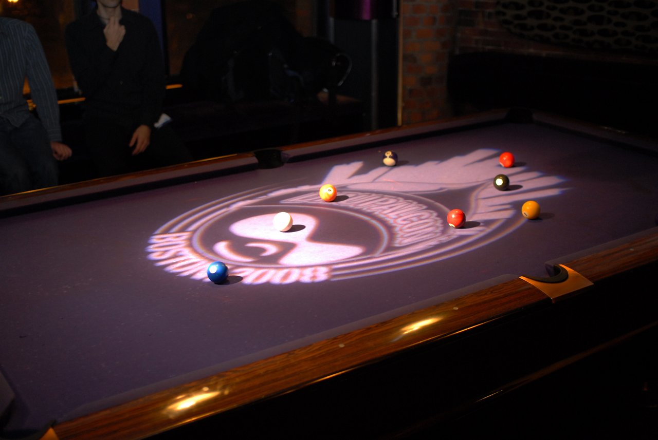 A pool table with scattered billiard balls and a DrupalCon Boston 2008 logo projected onto the surface.