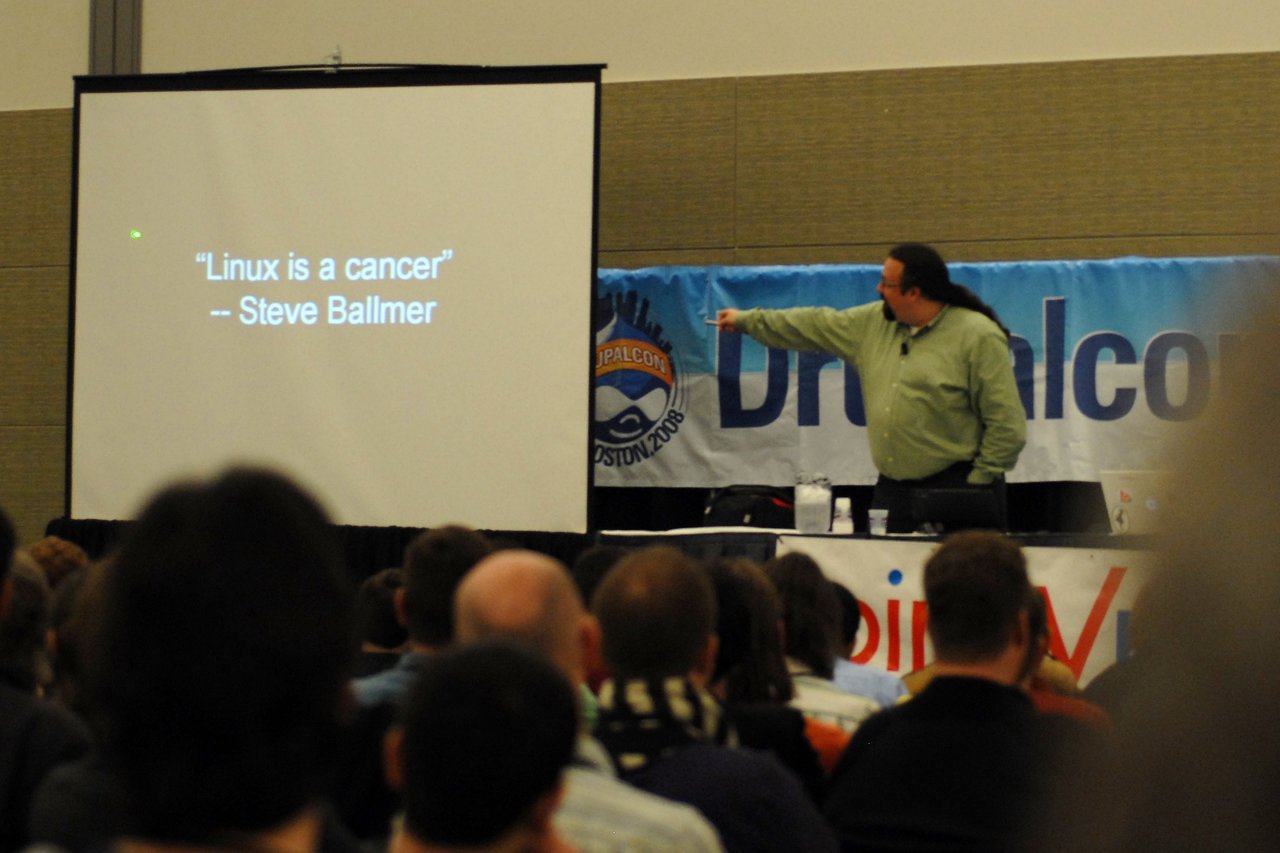Chris DiBona gives a presentation at DrupalCon Boston 2008, pointing at a slide quoting Steve Ballmer on Linux.