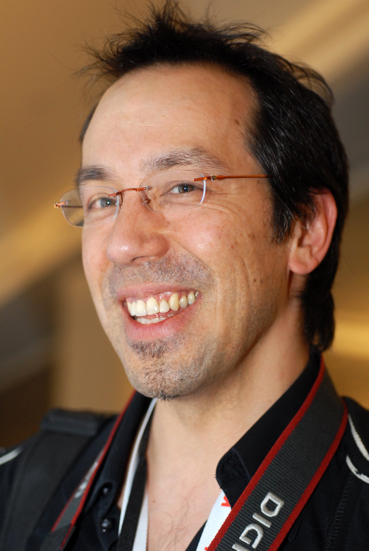 A smiling person wearing glasses and a camera strap around their neck at DrupalCon Boston 2008.