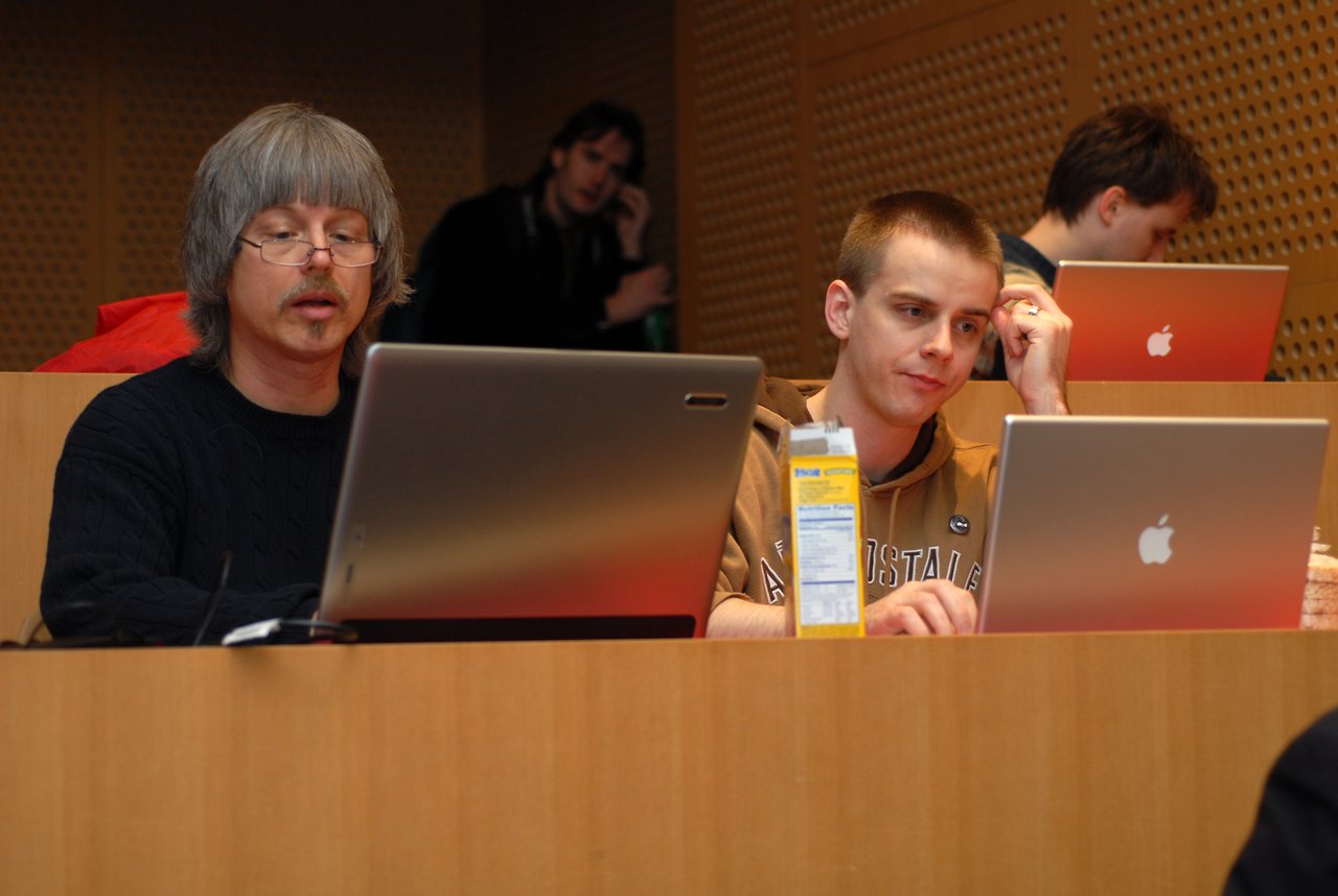 Two people sitting in a lecture hall, working on laptops.
