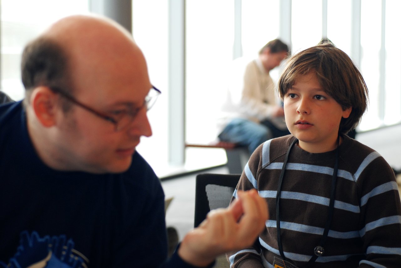 A man gestures while speaking to a young boy, who listens attentively at a DrupalCon Boston 2008 event.