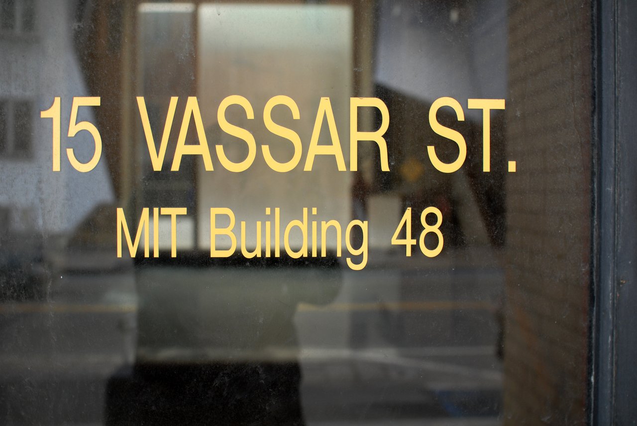 A glass door with gold lettering displaying "15 Vassar St.