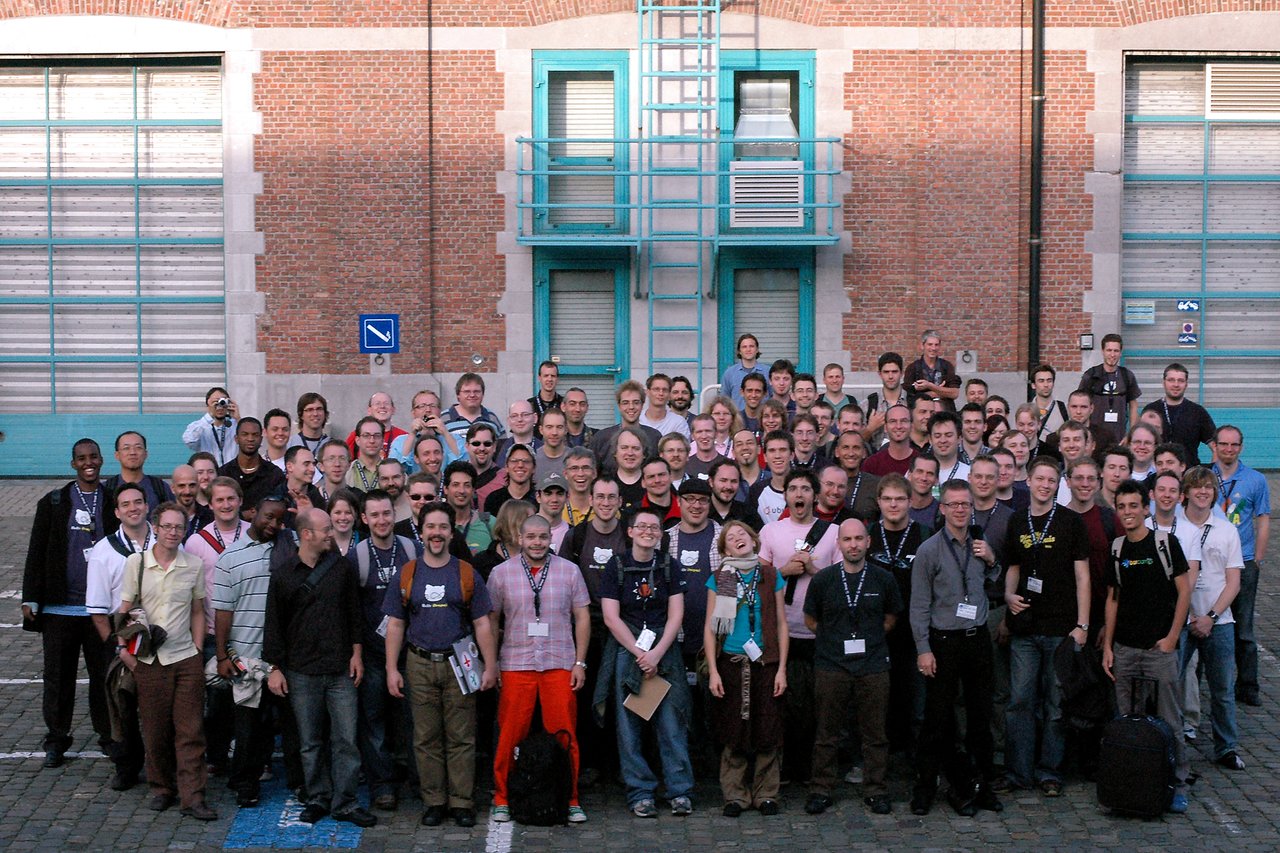 A large group of DrupalCon Brussels 2006 attendees gathers outside for a group photo, smiling and posing together.