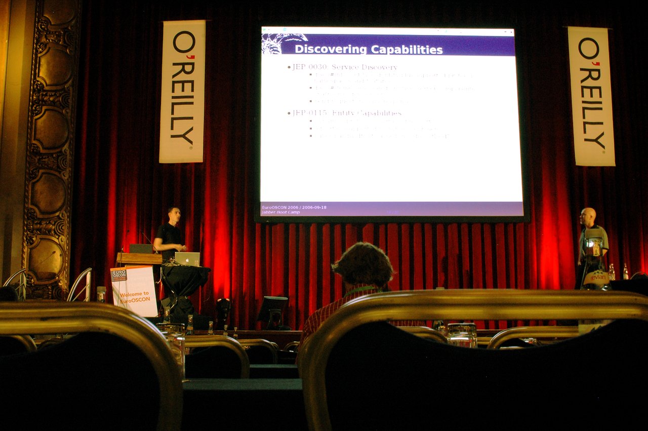 Two presenters discuss Jabber messaging on stage at EuroOSCON, with a large presentation slide behind them.