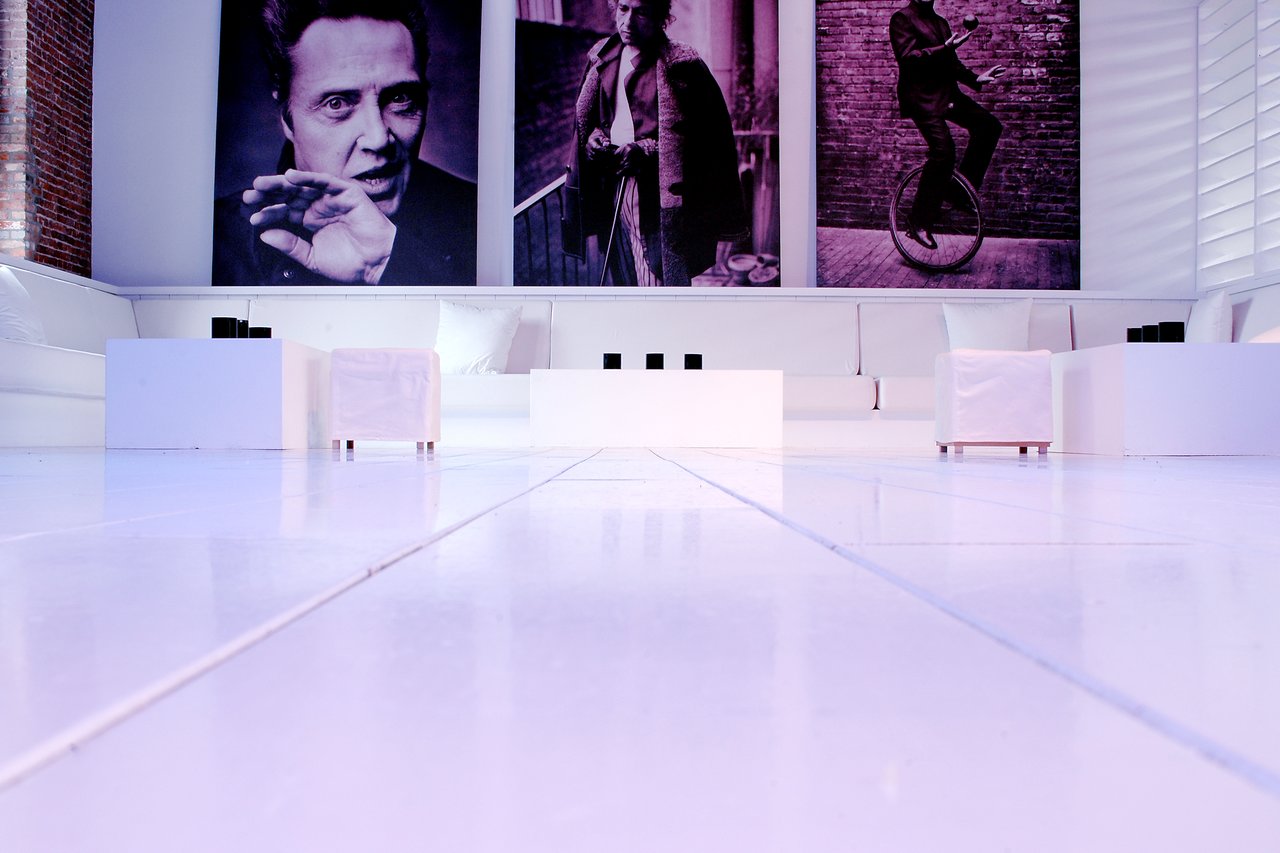 A modern lounge with white furniture, low tables, and large black-and-white portraits on the wall.