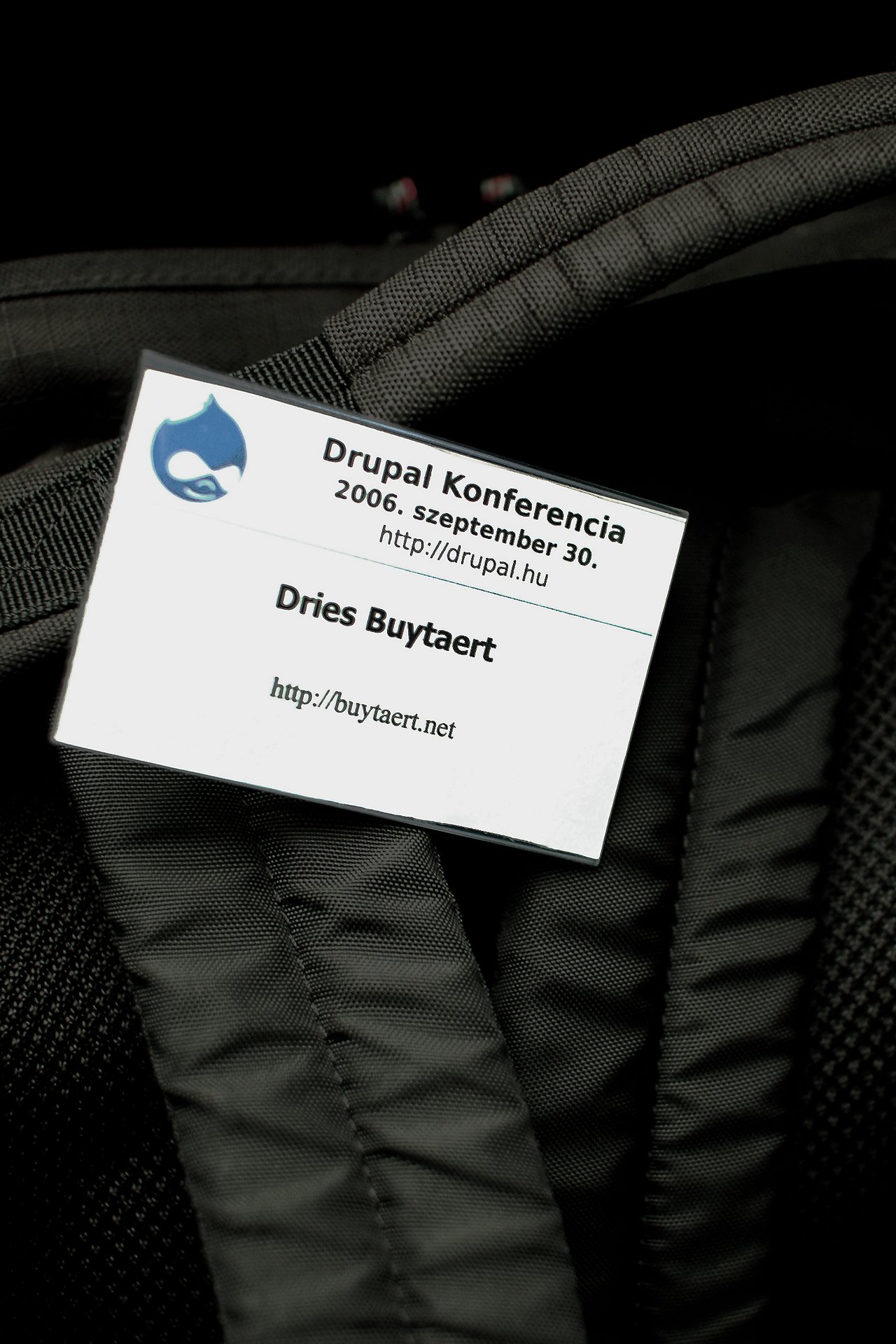 A Drupal Konferencia 2006 badge with a name and website, placed on a black fabric surface.