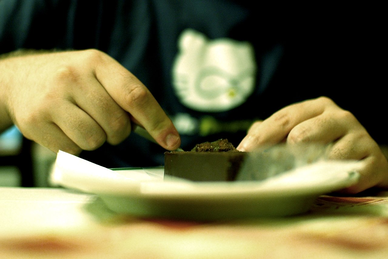 A person cuts a piece of chocolate cake on a plate with a knife.